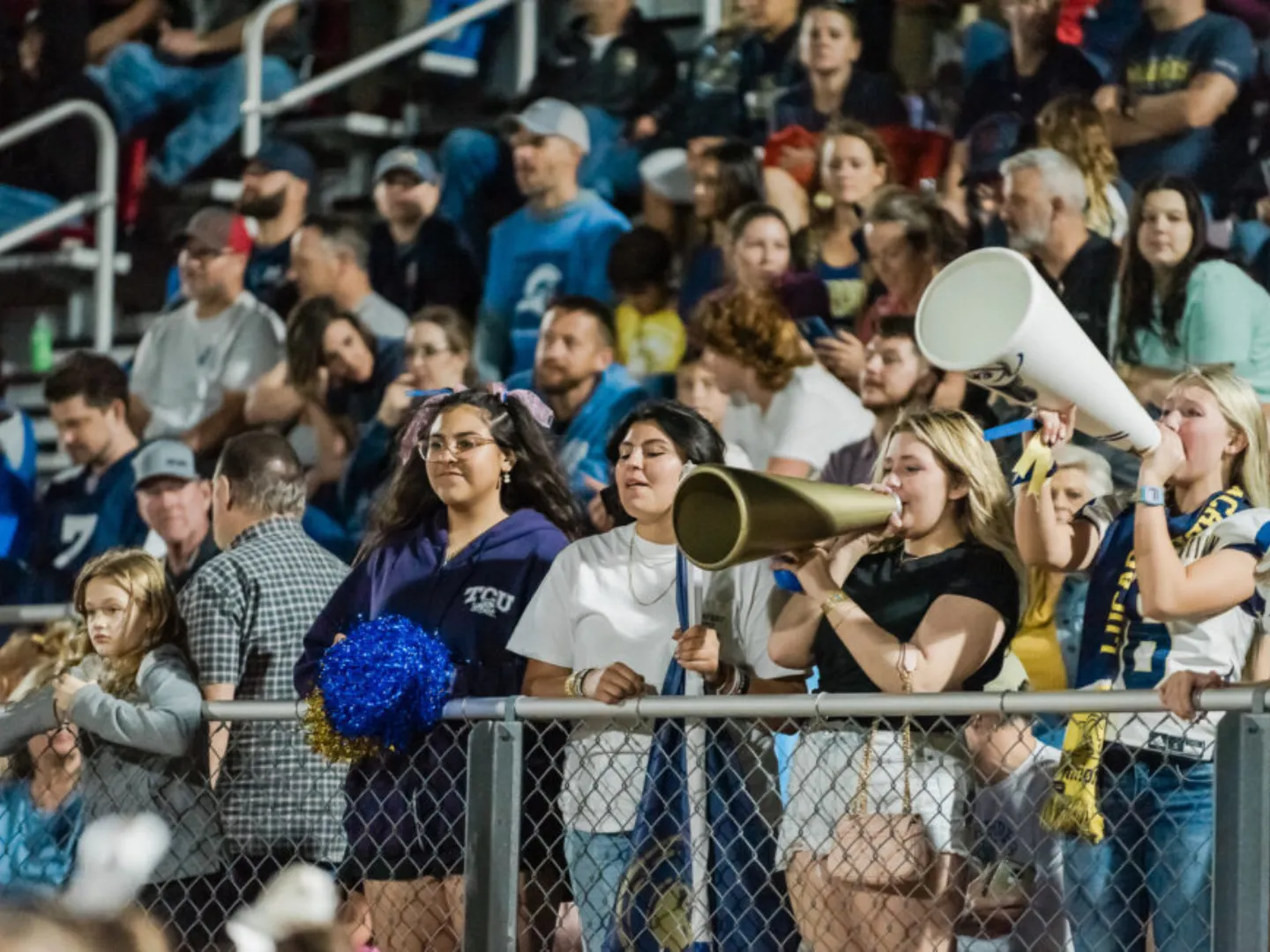 Lucas Christian Academy fans cheering with megaphones in the stands at a night football game