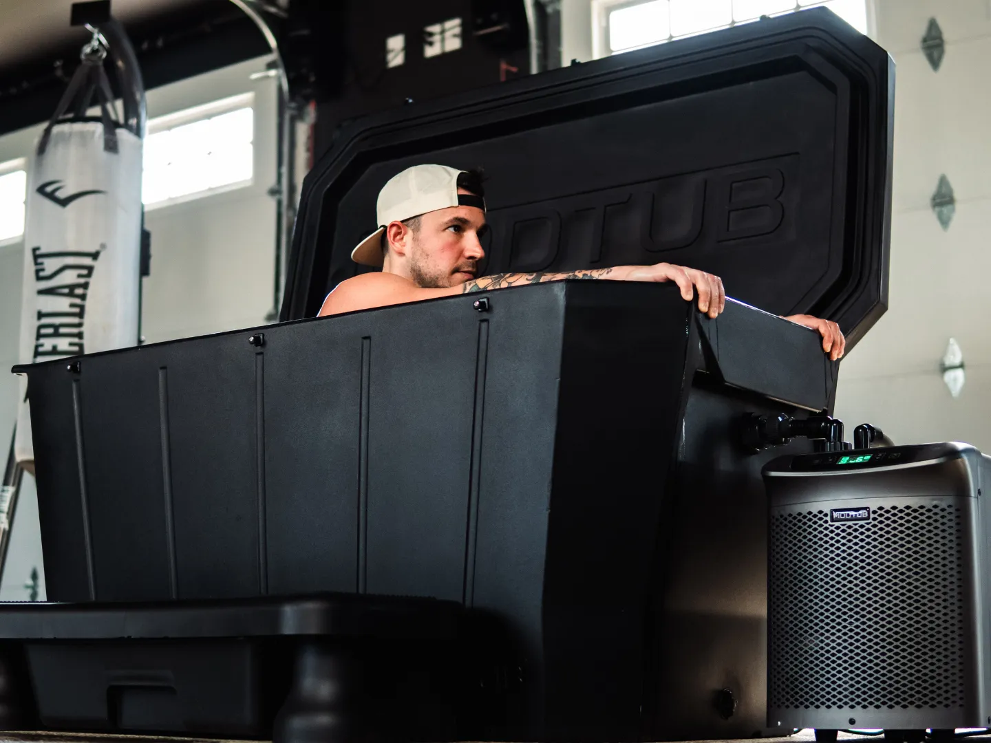 Man in a backwards cap leaning out of a Modtub cold plunge in a home gym